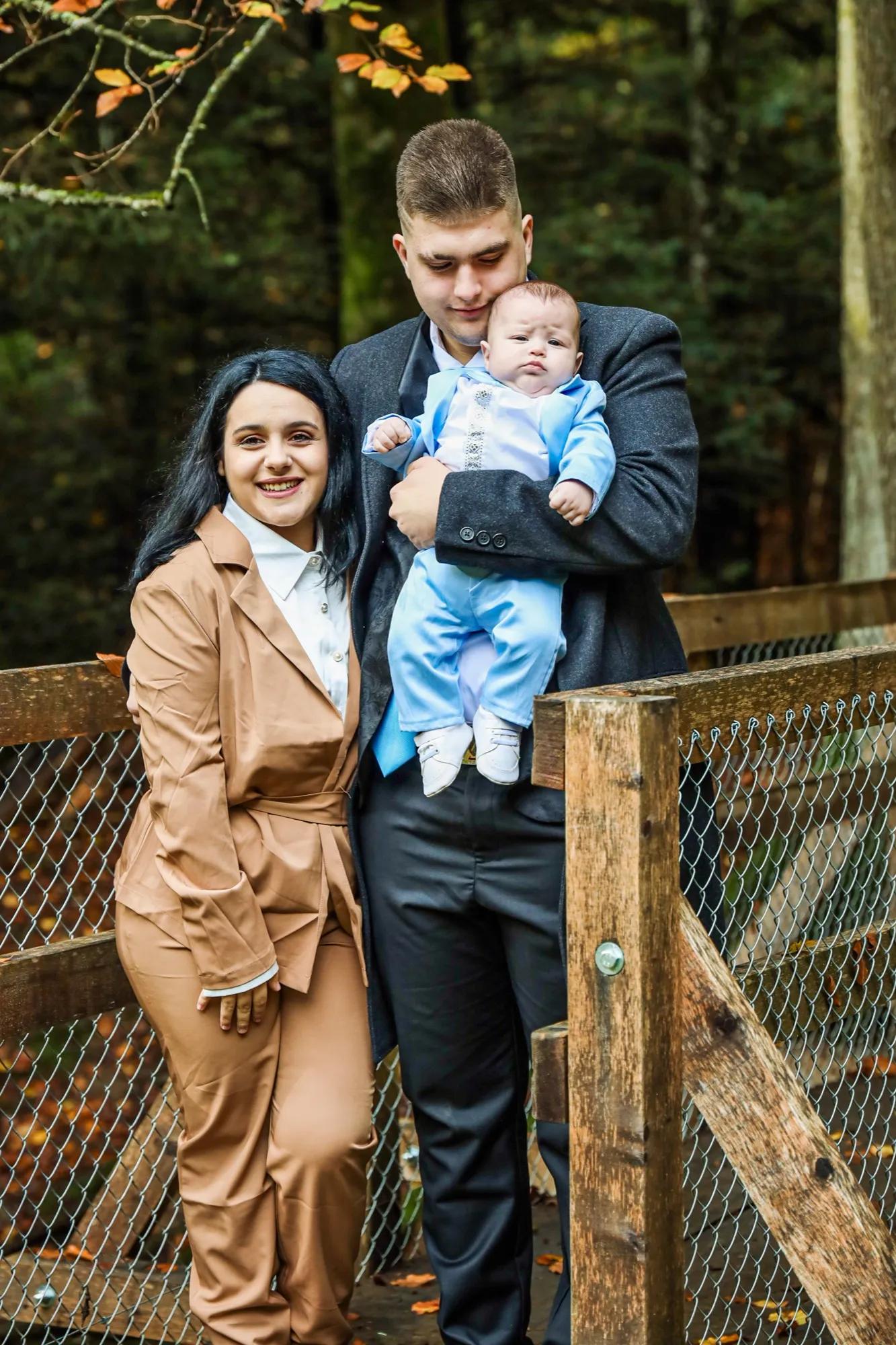 The parents and their baby in blue, in front of the forest