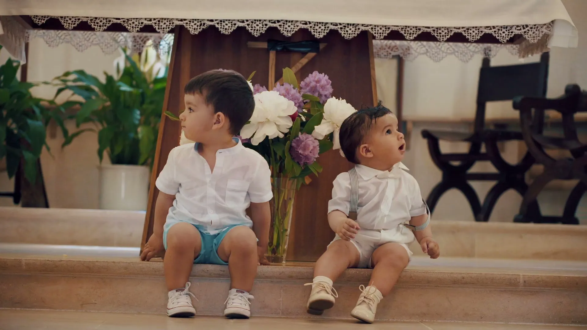 Two little boys dressed in white sitting on steps among flowers