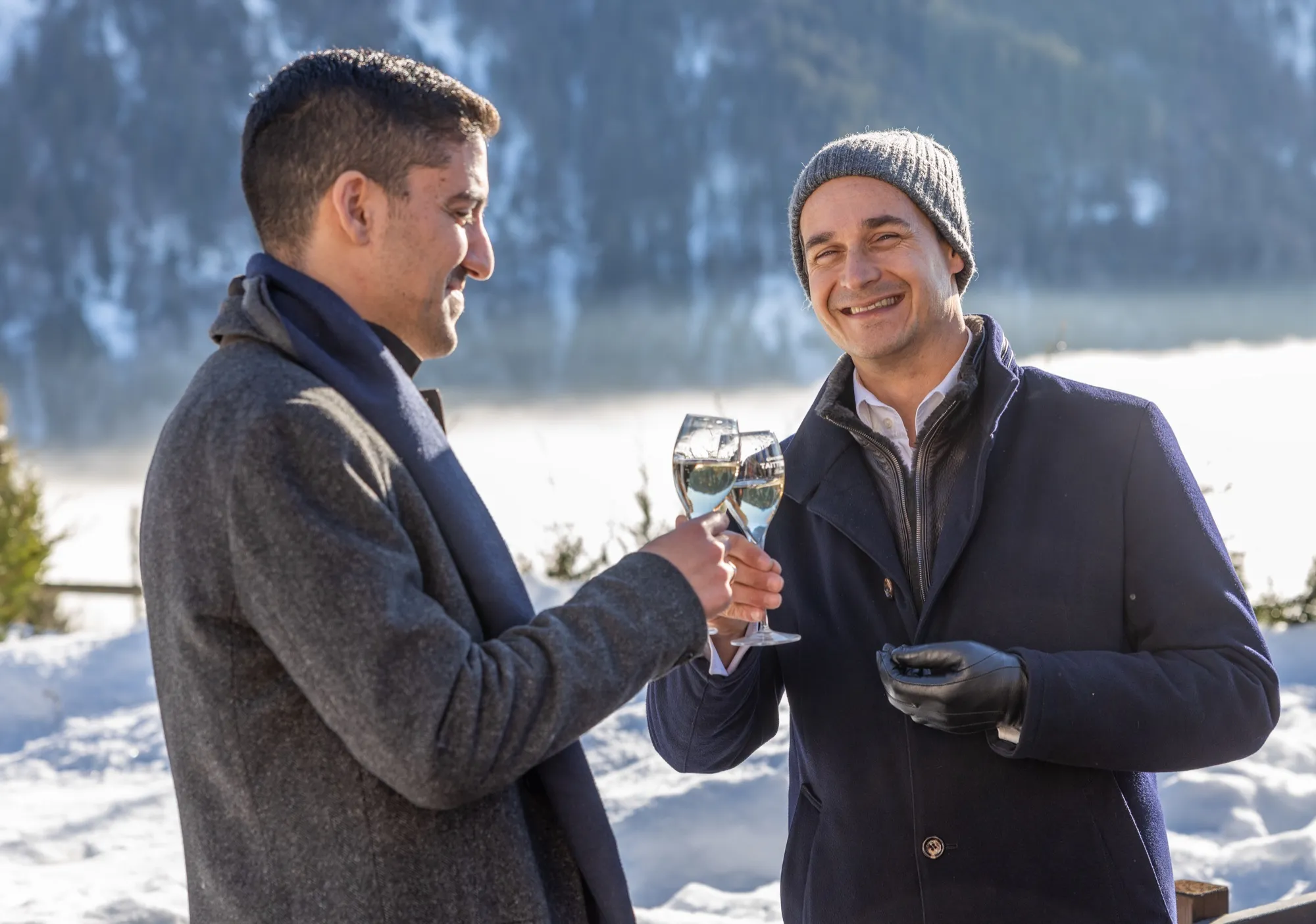 Two guests toasting with champagne by a snowy mountain lake