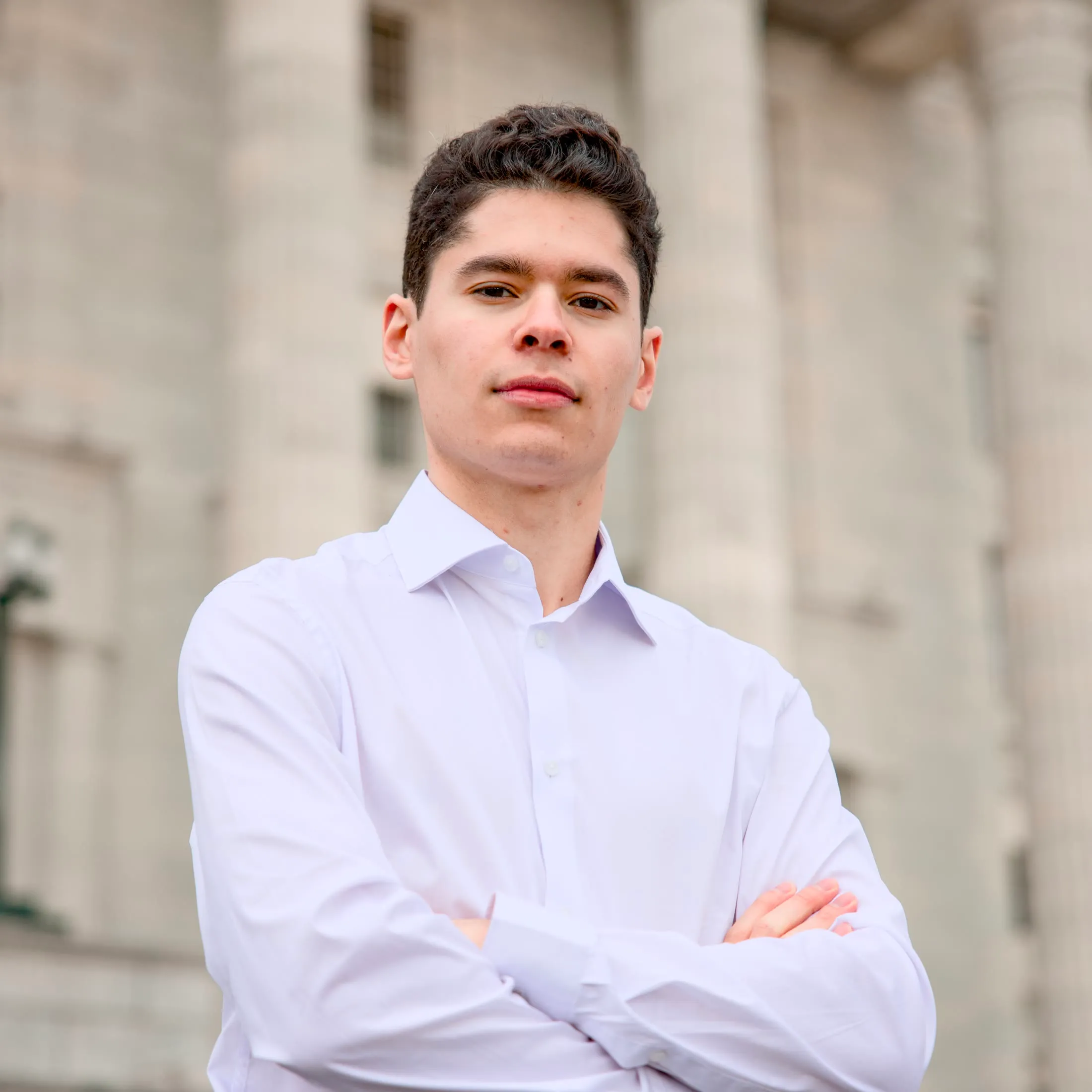 Portrait in a white shirt, arms crossed, in front of columns