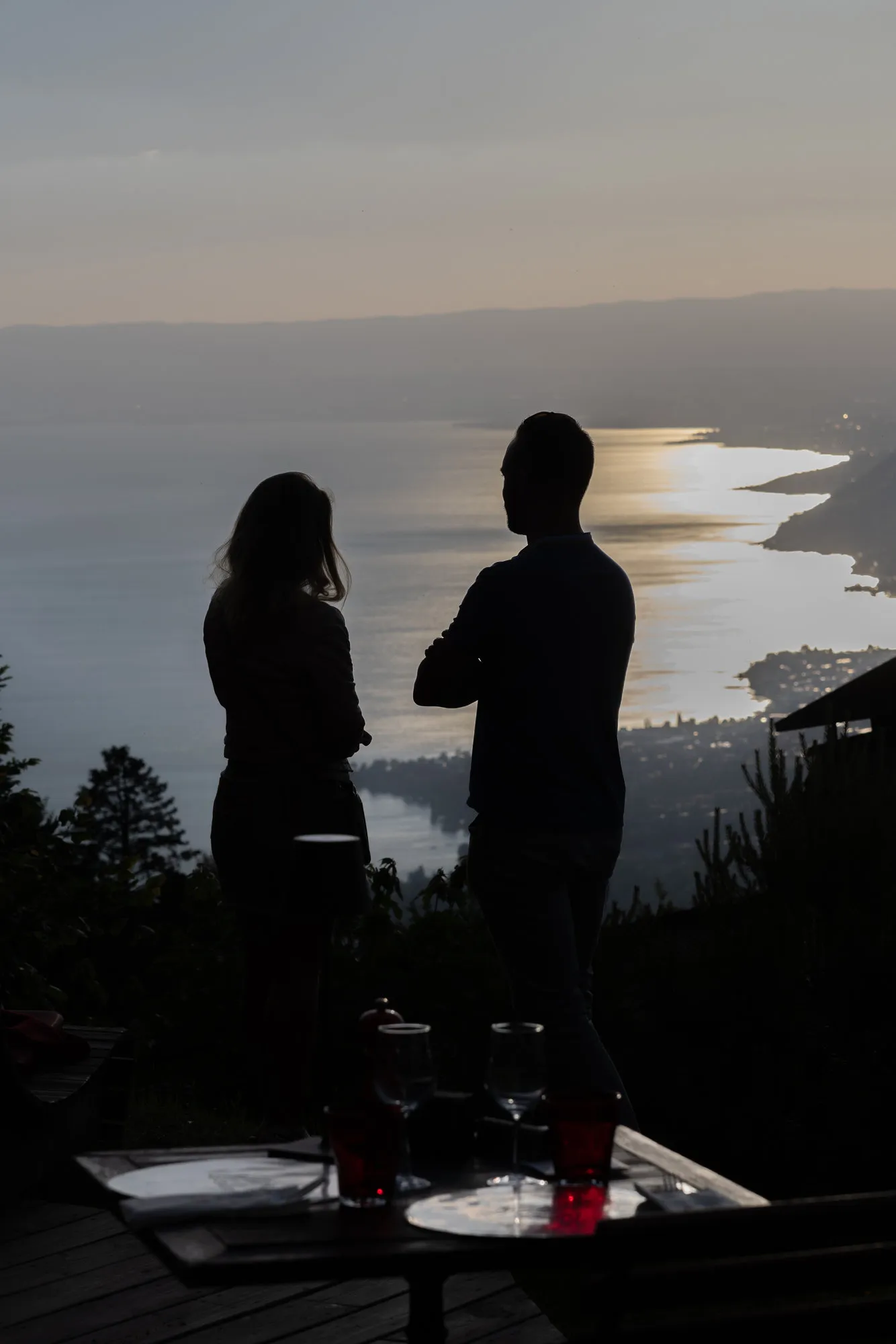 A couple in silhouette facing the lake at sunset